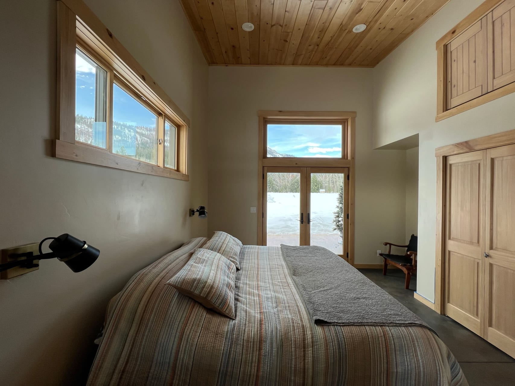 Guest bedroom with plaid bedding and French doors overlooking snow-covered mountains