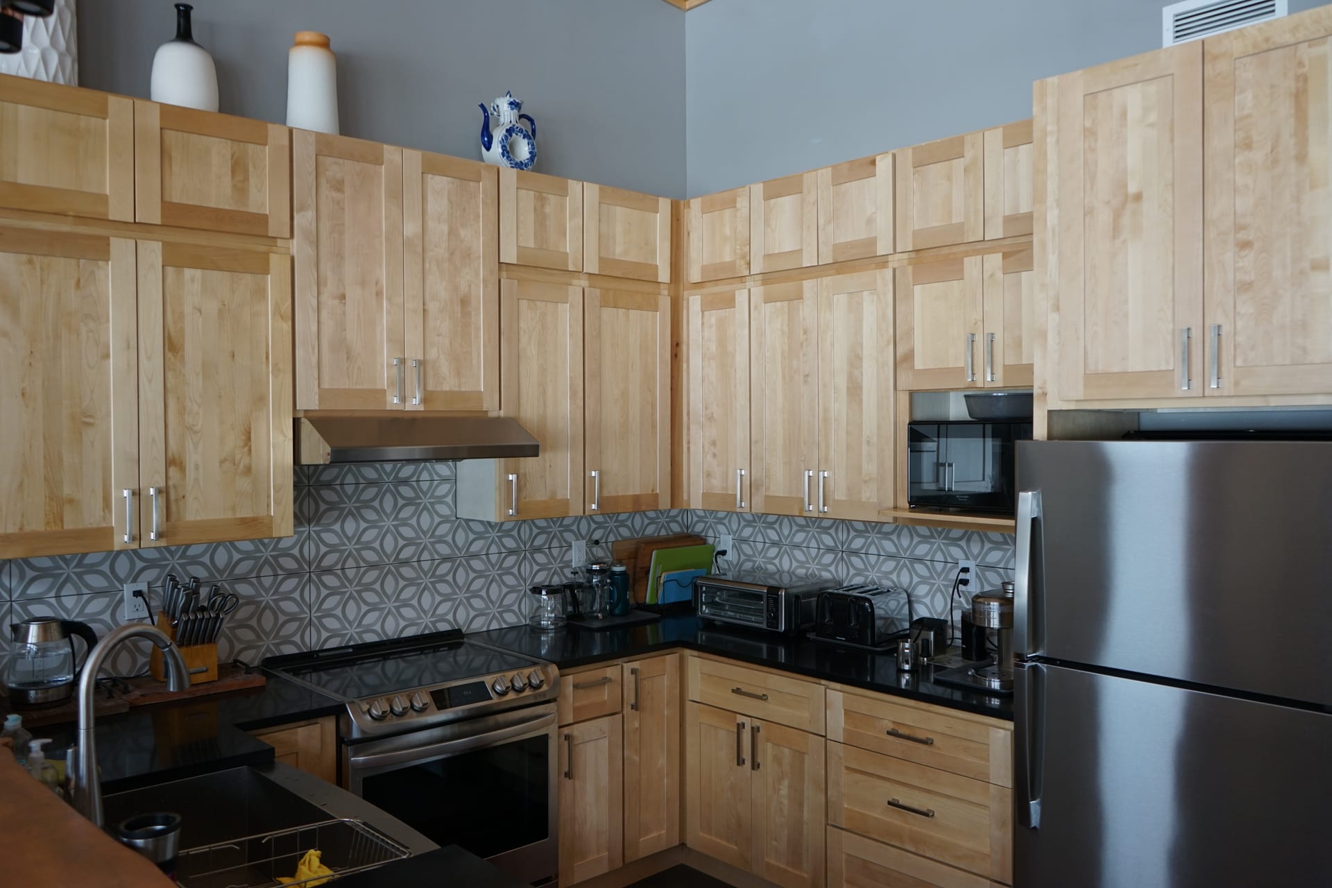 Kitchen with birch cabinetry, patterned tile backsplash, and black granite counters