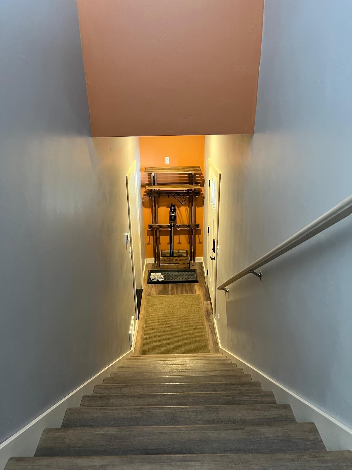 The staircase down from the apartment to its own entrance, a straight flight between grey walls to a terracotta entry hall with a coat rack at the bottom