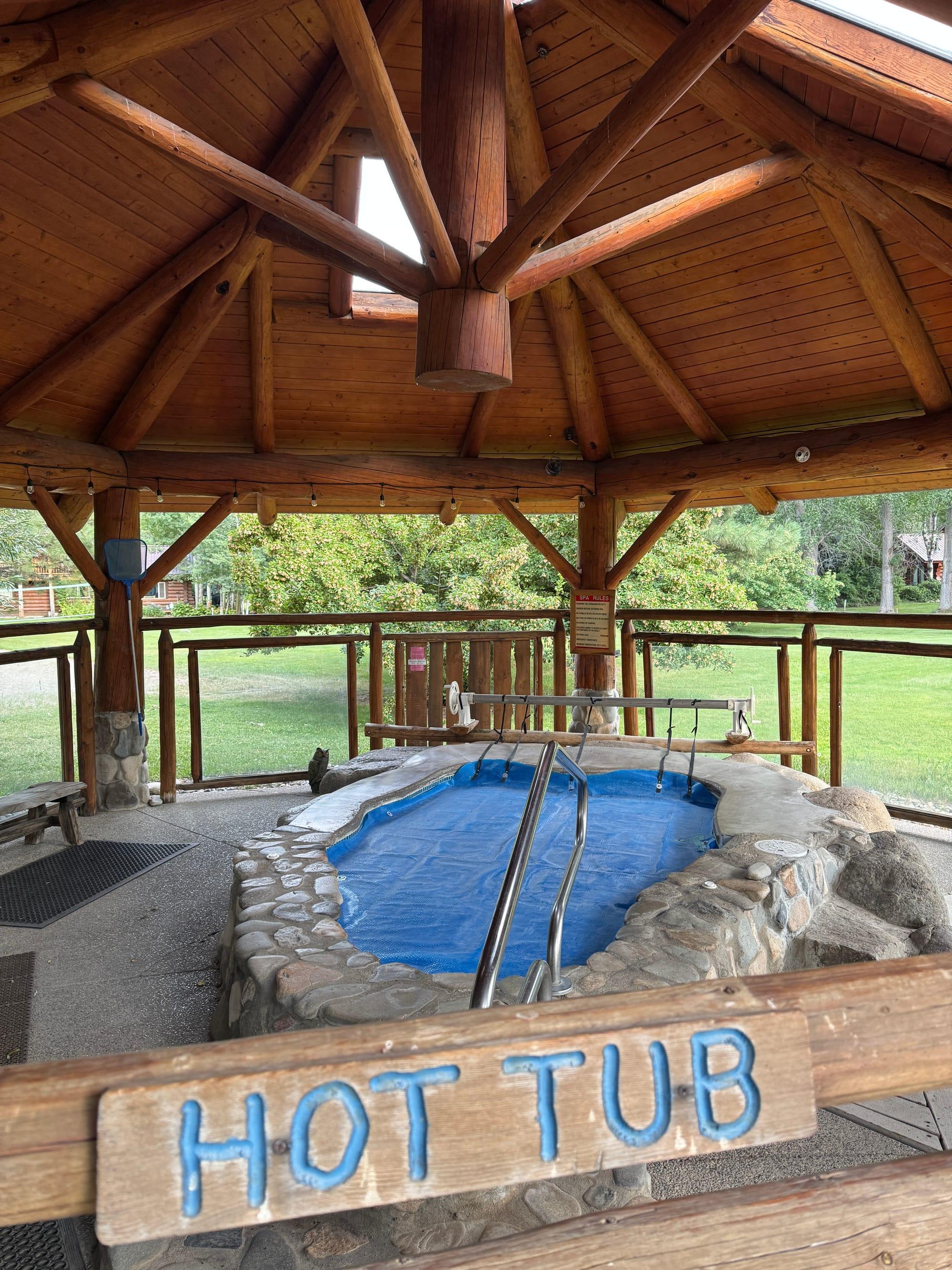 The shared hot tub under its log-framed shelter, set into a stone surround and open year round