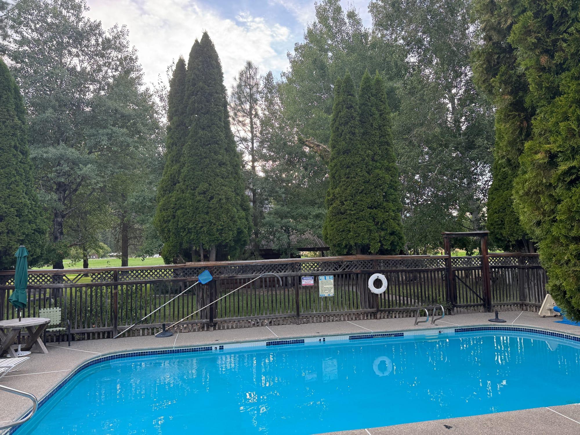 The community outdoor pool, fenced and set among cedars, looking out to the resort lawn