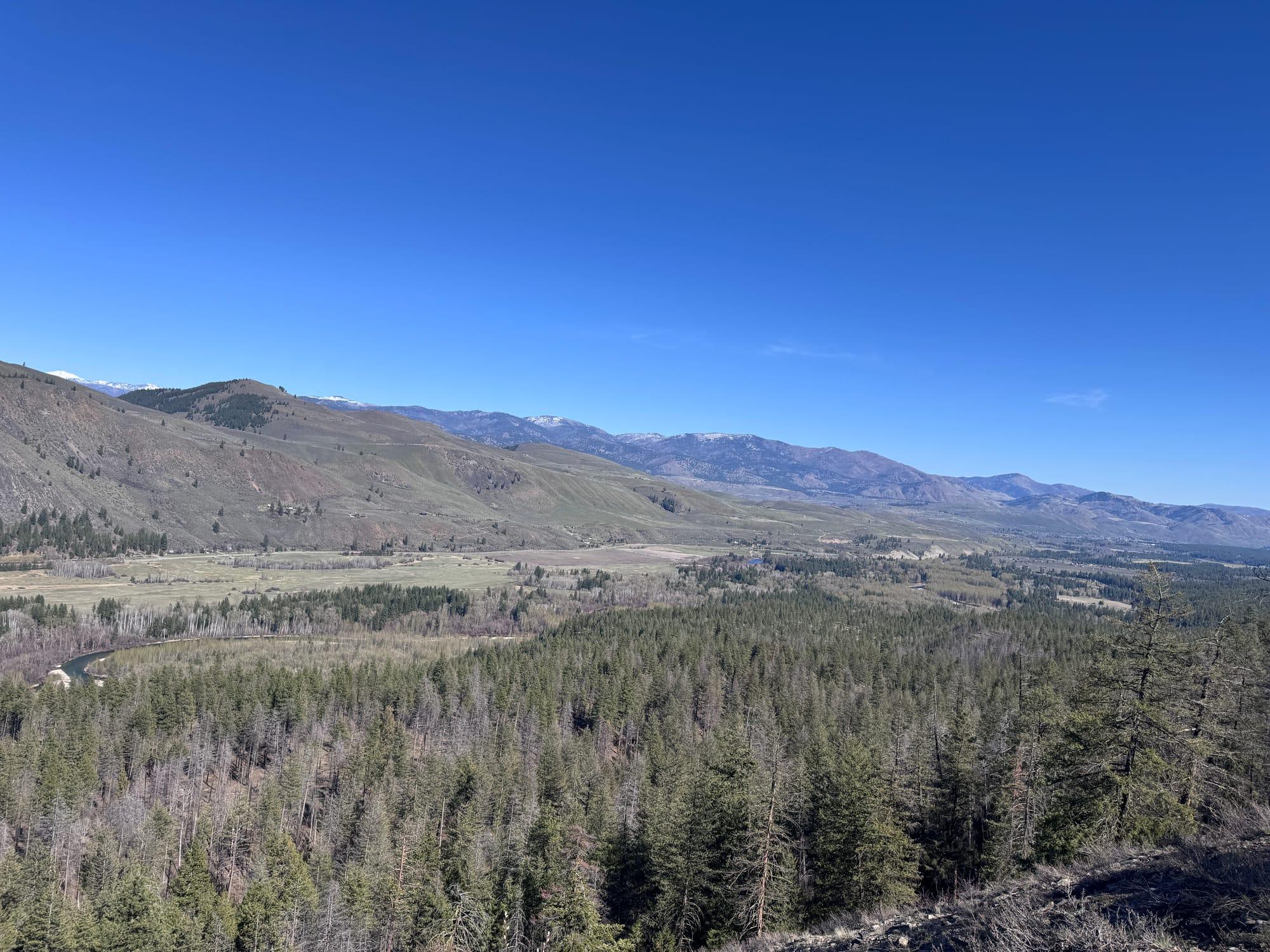 The whole valley from a high shoulder: forest, meadow and river running away to the mountains
