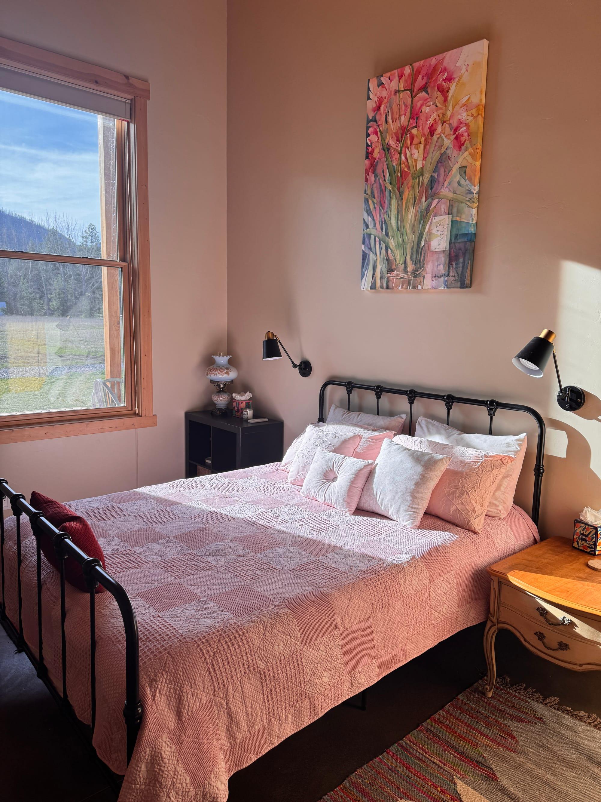 The guest bedroom: a black iron bedstead against a warm terracotta wall, with a window onto the meadow and the ridge beyond