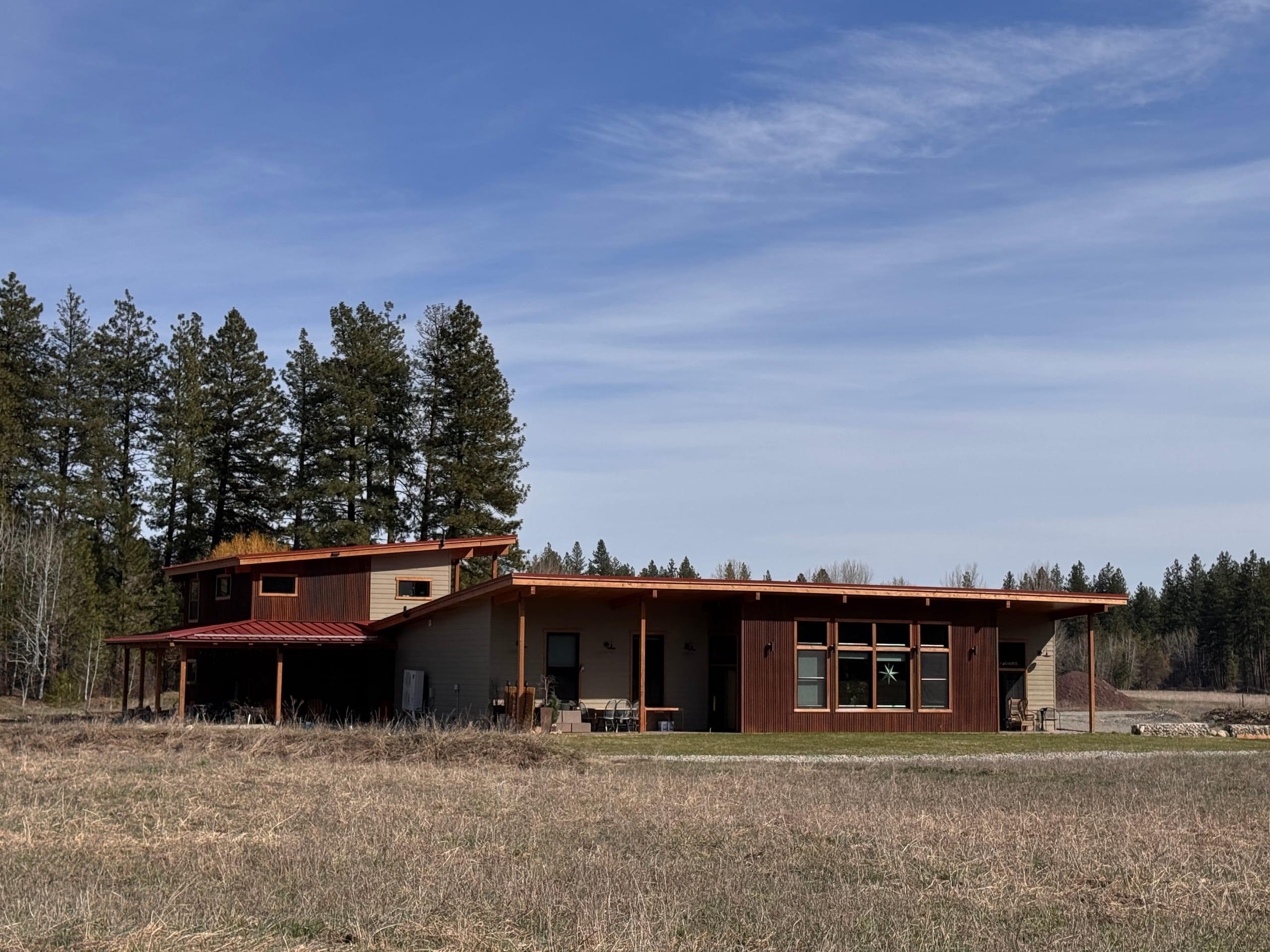 The house seen from the meadow: the long single-storey wing with its west-facing window wall on the right, and the two-storey garage and apartment block on the left, backed by ponderosa pines
