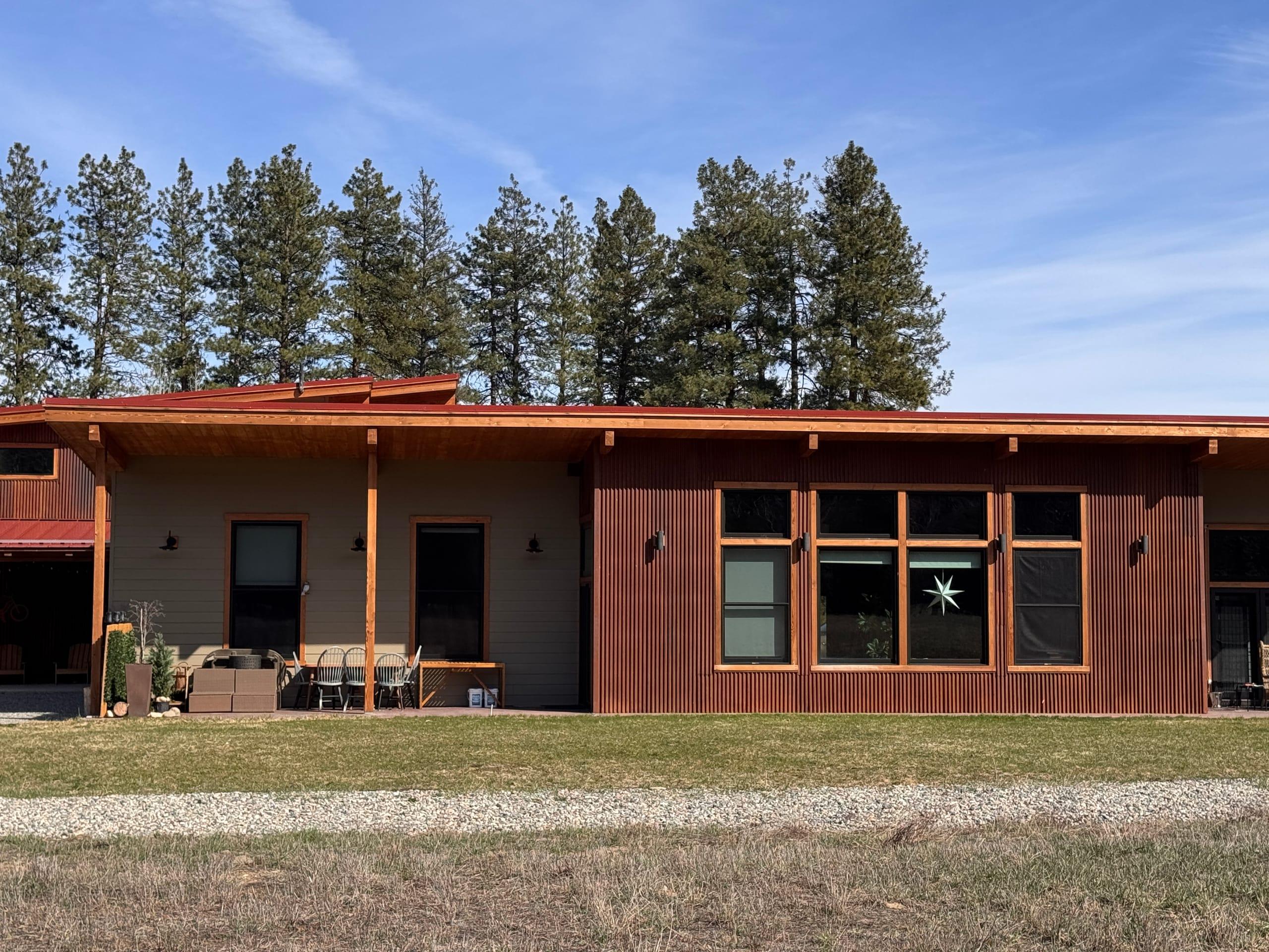 The west elevation close up: a wall of tall windows under a deep cedar-framed overhang, with the covered patio and dining table alongside